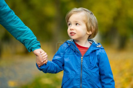 Photo for Funny toddler boy having fun outdoors on sunny autumn day. Child exploring nature. Kid holding mother's hand in a city park. Autumn activities for small kids. - Royalty Free Image