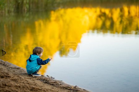 Photo for Adorable toddler boy having fun by the Gela lake on sunny fall day. Child exploring nature on autumn day in Vilnius, Lithuania. Fun autumn activities for kids. - Royalty Free Image
