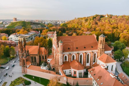 Téléchargez les photos : Vue aérienne de l'église Sainte-Anne et de l'église Bernardine voisine, l'un des bâtiments les plus beaux et probablement les plus célèbres de Vilnius. Belle journée d'automne dans la capitale de la Lituanie. - en image libre de droit