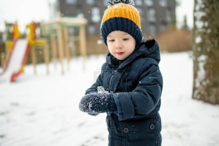 Photo for Adorable toddler boy having fun in a city on snowy winter day. Cute child wearing warm clothes playing in a snow. Winter activities for family with kids. - Royalty Free Image