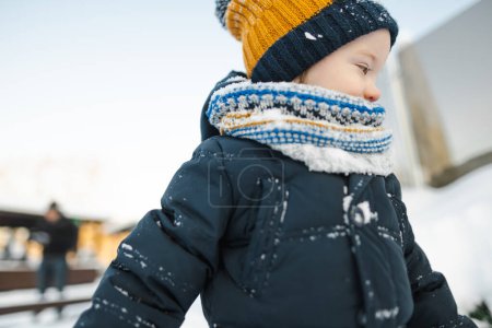 Foto de Adorable niño que se divierte en una ciudad en el día de invierno nevado. Lindo niño con ropa de abrigo jugando en una nieve. Actividades de invierno para la familia con niños. - Imagen libre de derechos