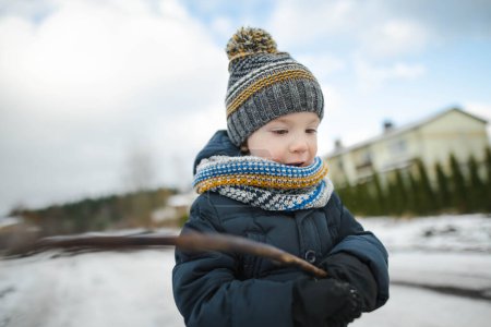 Photo for Adorable toddler boy having fun in a backyard on snowy winter day. Cute child wearing warm clothes playing in a snow. Winter activities for family with kids. - Royalty Free Image