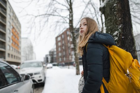 Téléchargez les photos : Jolie jeune fille avec un sac à dos se dirigeant vers l'école le matin froid d'hiver. Un enfant qui retourne à l'école. Éducation pour les enfants. - en image libre de droit