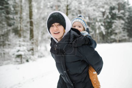 Foto de Adorable niño pequeño y su hermana mayor se divierten en un patio trasero en el día de invierno nevado. Lindo niño con ropa de abrigo jugando en una nieve. Actividades de invierno para la familia con niños. - Imagen libre de derechos