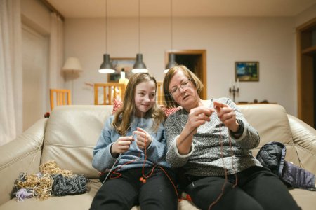 Photo for Grandmother and teenage granddaughter knitting on a sofa. Grandma teaching teen child to knit. Crafts and hobby for parents and kids. - Royalty Free Image