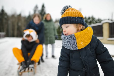 Foto de Divertido niño pequeño y sus hermanas mayores se divierten con un trineo en el hermoso parque de invierno. Lindo niño jugando en una nieve. Actividades de invierno para niños. - Imagen libre de derechos