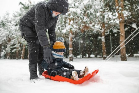 Téléchargez les photos : Petit garçon drôle s'amusant avec un traîneau dans un beau parc d'hiver. Mignon enfant jouant dans la neige. Activités hivernales pour les enfants. - en image libre de droit