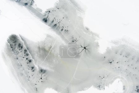 Téléchargez les photos : Vue aérienne du haut vers le bas de la surface gelée du lac en hiver, texture de la glace avec fissures, taches des cours d'eau sous-marins. Paysage hivernal pittoresque. - en image libre de droit