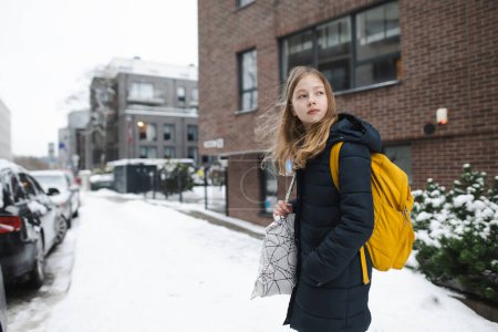 Foto de Linda joven con una mochila que se dirige a la escuela en la fría mañana de invierno. El niño vuelve a la escuela. Educación para niños. - Imagen libre de derechos
