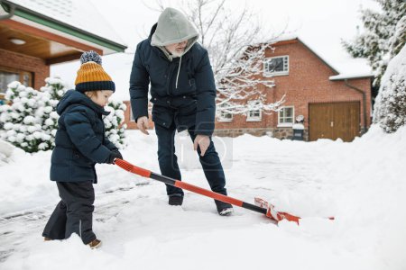 Photo for Adorable toddler boy helping his grandfather to shovel snow in a backyard on winter day. Cute child wearing warm clothes playing in a snow. Winter activities for family with kids. - Royalty Free Image