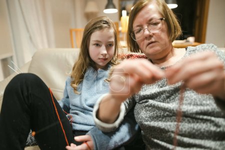 Téléchargez les photos : Grand-mère et petite-fille adolescente tricotant sur un canapé. Grand-mère enseigne à un adolescent à tricoter. Artisanat et passe temps pour les parents et les enfants. - en image libre de droit
