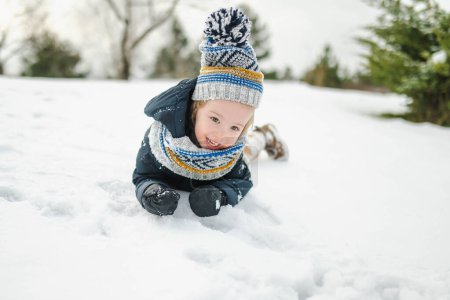 Photo for Adorable toddler boy having fun in a backyard on snowy winter day. Cute child wearing warm clothes playing in a snow. Winter activities for family with kids. - Royalty Free Image