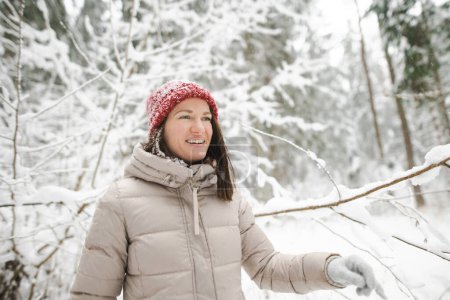 Foto de Mujer joven divirtiéndose en un paseo por el bosque de pinos cubierto de nieve en el frío día de invierno. Senderista explorando la naturaleza. Actividades de invierno para adultos. - Imagen libre de derechos
