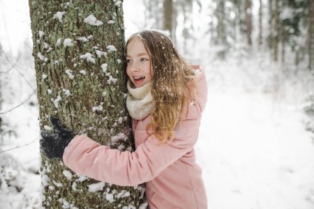 Foto de Linda chica adolescente divirtiéndose en un paseo por el bosque de pinos cubierto de nieve en el frío día de invierno. Niño adolescente explorando la naturaleza. Actividades de invierno para niños. - Imagen libre de derechos