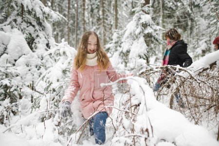 Foto de Divertidas hermanas adolescentes divirtiéndose en un paseo por el bosque de pinos cubierto de nieve en el frío día de invierno. Adolescentes explorando la naturaleza. Actividades de invierno para niños. - Imagen libre de derechos