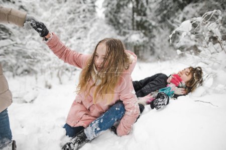 Téléchargez les photos : Funny sœurs adolescentes et leur mère s'amusent lors d'une promenade dans la forêt de pins enneigée par une journée d'hiver fraîche. Les adolescentes explorent la nature. Activités hivernales pour les enfants. - en image libre de droit