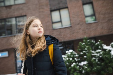 Téléchargez les photos : Jolie jeune fille avec un sac à dos se dirigeant vers l'école le matin froid d'hiver. Un enfant qui retourne à l'école. Éducation pour les enfants. - en image libre de droit