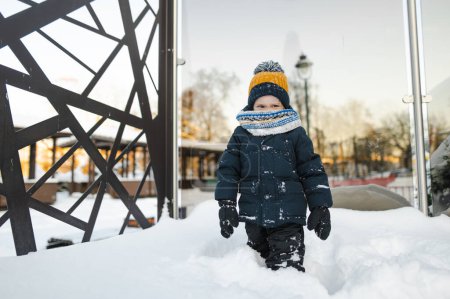 Photo for Adorable toddler boy having fun in a city on snowy winter day. Cute child wearing warm clothes playing in a snow. Winter activities for family with kids. - Royalty Free Image