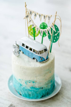 Téléchargez les photos : Gâteau d'anniversaire pour tout-petit de trois ans, décoré avec des arbres en papier et un petit bus. Gâteau maison sur le thème de la voiture pour la célébration d'anniversaire avec petite bannière et glaçage blanc et bleu. - en image libre de droit