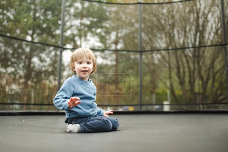 Photo for Cute little boy jumping on a trampoline in a backyard on warm and sunny summer day. Sports and exercises for children. Summer outdoor leisure activities. - Royalty Free Image