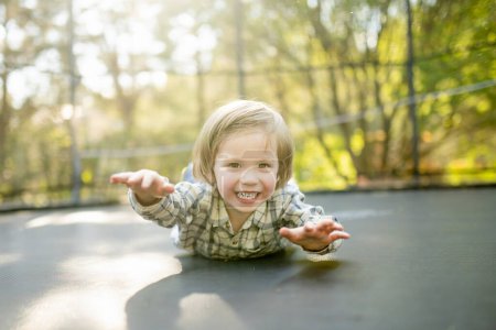 Foto de Lindo niño saltando en un trampolín en un patio trasero en el día de verano cálido y soleado. Deportes y ejercicios para niños. Actividades de ocio al aire libre de verano. - Imagen libre de derechos