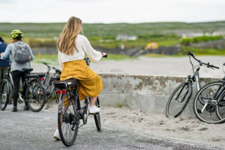 Foto de INISHMORE, IRLANDA - 21 MAY, 2023: Chica turística montando bicicleta eléctrica en Inishmore, la más grande de las Islas Aran en Galway Bay, Irlanda. - Imagen libre de derechos