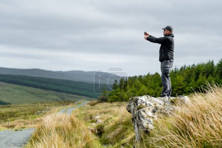 Foto de Turista tomando una foto en Glengesh Pass, impresionante carretera de paso de montaña en el oeste de Donegal entre la ciudad histórica de Ardara y el encantador pueblo de Glencolumbcille, Donegal, Irlanda. - Imagen libre de derechos