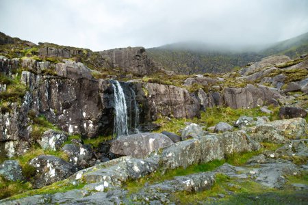 Photo for Small waterfall at the Conor Pass, one of the highest Irish mountain passes served by an asphalted road, located on the south-western end of the Dingle Peninsula, County Kerry, Ireland - Royalty Free Image