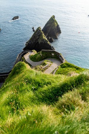 Photo for Dunquin or Dun Chaoin pier, Ireland's Sheep Highway. Narrow pathway winding down to the pier, ocean coastline, cliffs. Popular iconic location on Slea Head Drive and Wild Atlantic Way. - Royalty Free Image