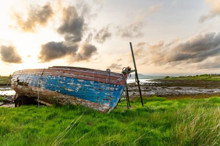 Foto de Barco viejo a la izquierda en una pequeña playa a lo largo de la ruta Ring of Kerry. Rugged coast of on Iveragh Peninsula on sunset, County Kerry, Irlanda
. - Imagen libre de derechos