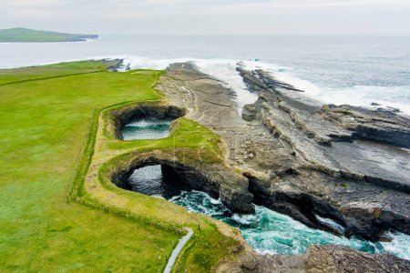 Aerial view of Bridges of Ross, three natural rock arches, carved into the cliffs by natural ocean erosion, on the west coast of Ross Bay, Wild Atlantic Way Discovery Point, County Clare, Ireland