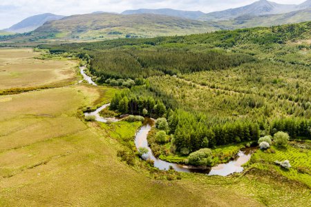 Luftaufnahme des sich unten schlängelnden Flusses Joyce in der Region Connemara in Irland. Landschaftlich reizvolle irische Landschaft mit herrlichen Bergen am Horizont, County Galway, Irland.