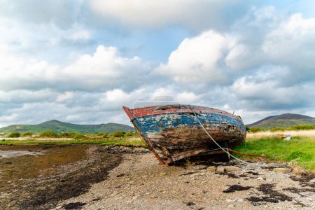 Old boat left on a small beach along the Ring of Kerry route. Rugged coast of on Iveragh Peninsula on sunset, County Kerry, Ireland.
