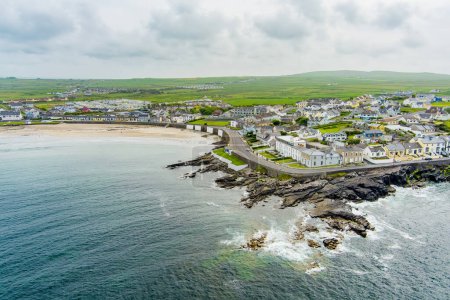 Foto de Vista aérea de Kilkee, pequeña ciudad costera, popular como balneario, ubicada en la bahía de herradura y protegida del Océano Atlántico por el arrecife de Duggerna, condado de Clare, Irlanda. - Imagen libre de derechos