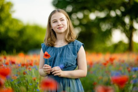 Téléchargez les photos : Belle adolescente admirant les fleurs de pavot et de potamot dans un champ de pavot en fleurs le jour d'été ensoleillé. Beaux paysages d'été près de Vilnius, Lituanie. - en image libre de droit