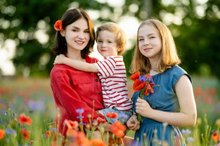 Téléchargez les photos : Belles adolescentes et leur petit frère admirant les fleurs de pavot et de potamot dans un champ de pavot en fleurs le jour ensoleillé de l'été. - en image libre de droit