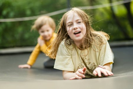 Téléchargez les photos : Mignon tout-petit garçon et sa sœur sautant sur un trampoline dans un jardin. Sports et exercices pour les enfants. Activités de plein air estivales. - en image libre de droit