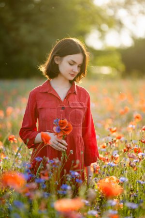 Téléchargez les photos : Belle adolescente admirant les fleurs de pavot et de potamot dans un champ de pavot en fleurs le jour d'été ensoleillé. Beaux paysages d'été près de Vilnius, Lituanie. - en image libre de droit