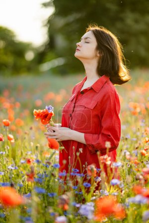 Photo for Beautiful teenage girl admiring poppy and knapweed flowers in blossoming poppy field on sunny summer day. Beautiful summer scenery near Vilnius, Lithuania. - Royalty Free Image