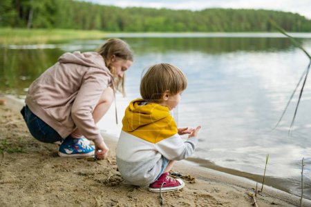Photo for Cute little boy and his sister playing by a lake or river on hot summer day. Adorable child having fun outdoors during summer vacations. Water activities for kids. - Royalty Free Image