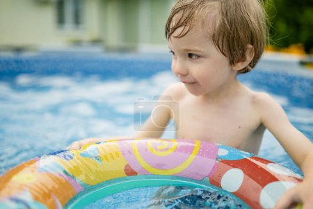 Téléchargez les photos : Cuty drôle garçon tout-petit s'amuser dans la piscine extérieure. Enfant apprenant à nager. Le gamin s'amuse avec des jouets aquatiques. Amusement en famille dans une piscine. Activités estivales pour la famille avec enfants. - en image libre de droit