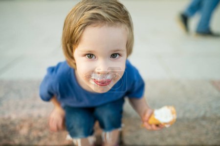 Foto de Lindo niño comiendo sabroso helado fresco al aire libre en el cálido día soleado de verano en Vilna, Lituania. Niño comiendo dulces. Alimento poco saludable para niños. - Imagen libre de derechos