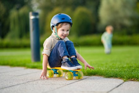 Photo for Cute little boy learning to skateboard on beautiful summer day in a park. Child wearing safety helmet enjoying skateboarding ride outdoors. Active leisure for small kids. - Royalty Free Image