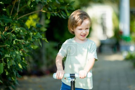 Foto de Adorable niño montado en su scooter en un patio trasero en la soleada noche de verano. Un niño pequeño montando un rodillo. Ocio activo y deportes al aire libre para niños. - Imagen libre de derechos