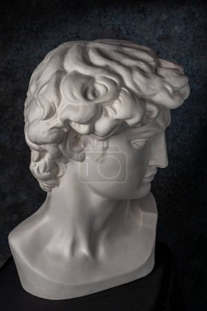 Gypsum copy of head statue David for artists on dark background. Replica of face famous sculpture youth of David by Michelangelo. Renaissance epoch. Template design for art, dj, fashion, poster, zine.