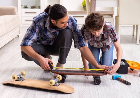 Téléchargez les photos : Le jeune père réparant skateboard avec son fils à la maison - en image libre de droit