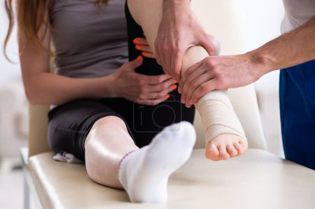 Foto de La mujer lesionada de la pierna visitando al joven médico traumatólogo - Imagen libre de derechos