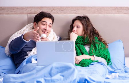 Foto de La esposa enferma y el marido en la cama con el portátil - Imagen libre de derechos