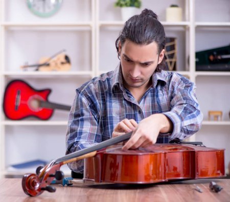 Téléchargez les photos : Le jeune beau réparateur réparant violoncelle - en image libre de droit