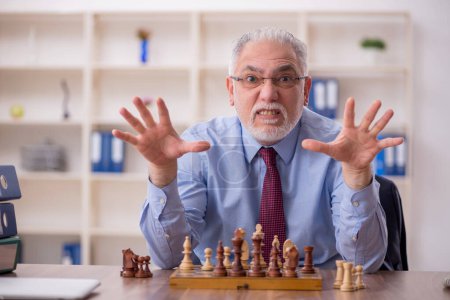 Téléchargez les photos : Vieil employé masculin jouant aux échecs dans le bureau - en image libre de droit